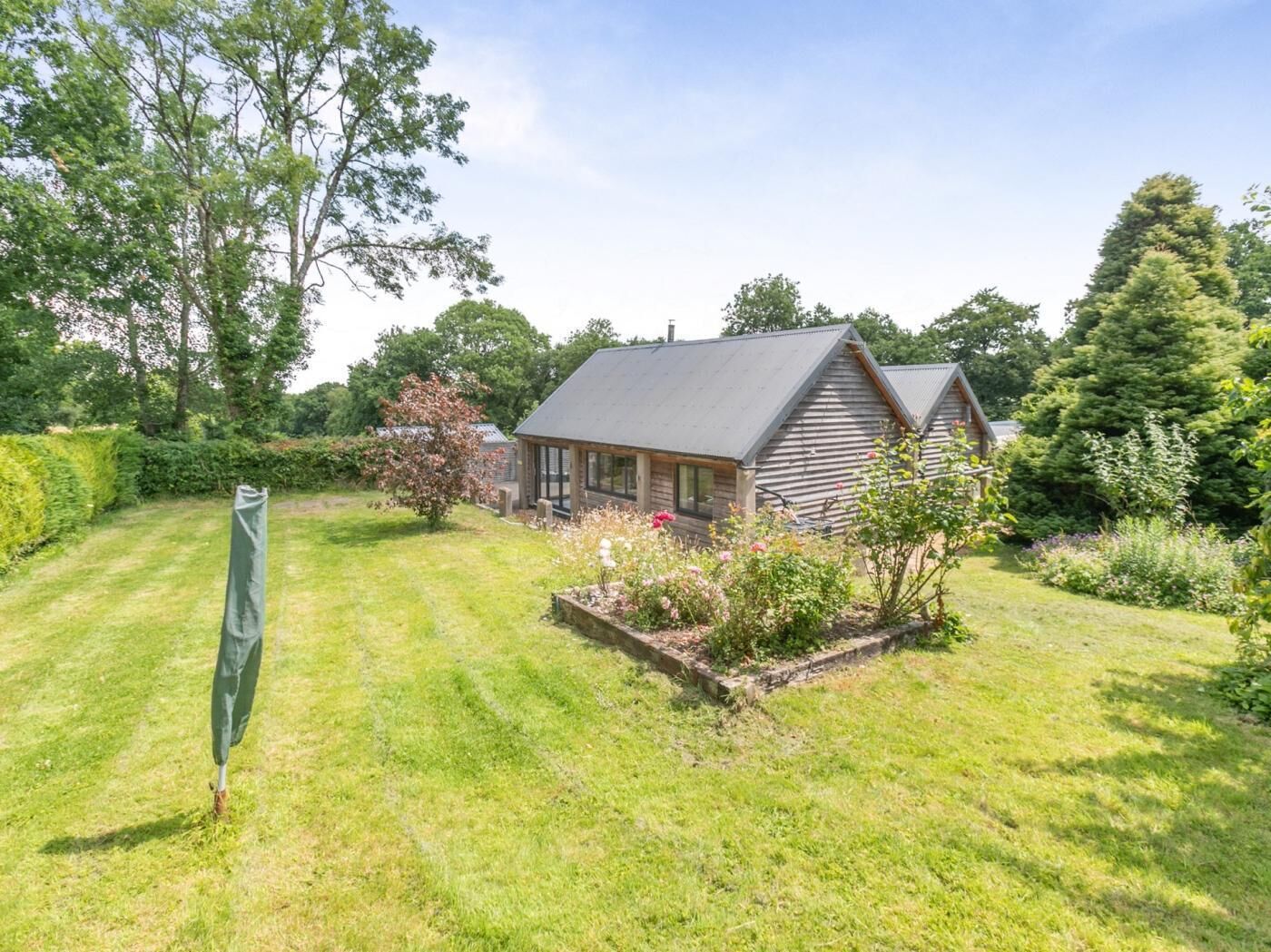 A wooden cabin with a sloped roof, surrounded by a well-maintained lawn and various flowering plants.