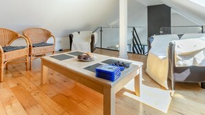 Un loft modern amb sòl de fusta, una taula de dinar amb un plat de galetes, dues cadires de vimetla, un sofà i una escala.