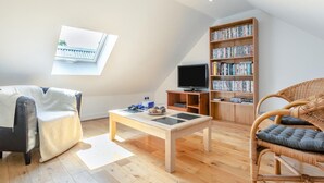 Un saló d'estil loft amb un sostre alçat, un fanal, una televisió, una prestatgeria, una taula de centre i dues cadires.