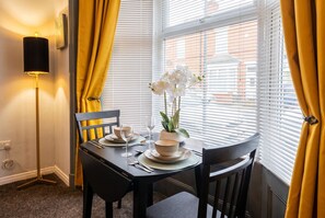 A dining area with a table set for two, a floor lamp, and a window with blinds.