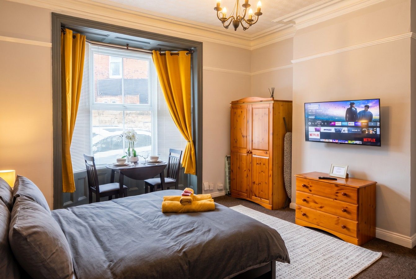 Studio room with a double bed, pine wardrobe, smart TV and bay-window dining set.