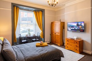 A hotel room with a bed, a TV, a wooden wardrobe, and a window with curtains.