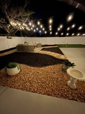 Ein Terrassenbereich im Freien mit einer Sitzgruppe, einem kleinen Kiesgarten und Lichterketten.