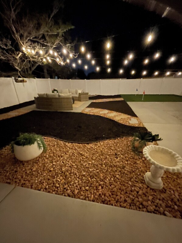 An outdoor patio area with a seating arrangement, a small garden with pebbles, and string lights.