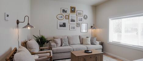 A living room with a sofa, armchair, coffee table, and wall-mounted picture frames.
