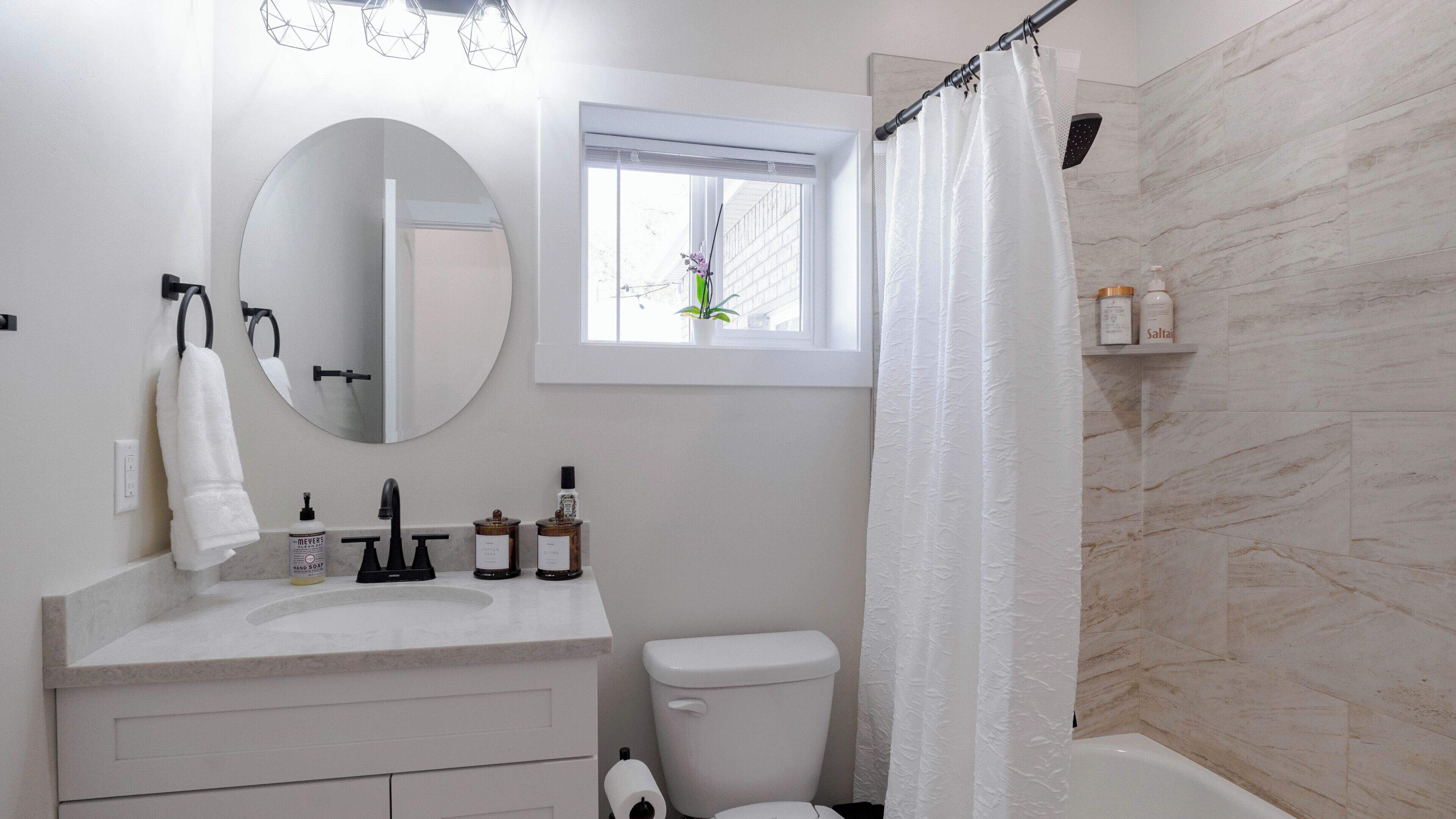 A bathroom with a white sink, a round mirror, a toilet, and a shower curtain.