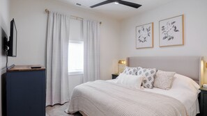 A bedroom with a bed, a desk, a television, and two framed floral artworks on the wall.