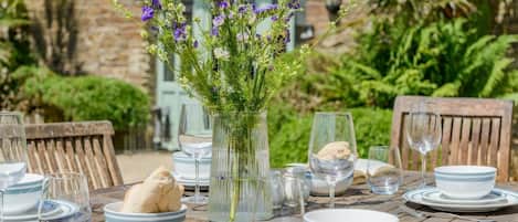 A wooden table set for dining with plates, bowls, glasses, and a vase with purple flowers.