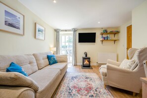 Ein Wohnzimmer mit Sofa, Sessel, Teppich, Kamin, Fernseher und Bücherregalen.