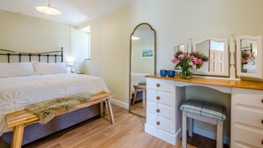 Quarto com cama, mesa de cabeceira, cômoda, espelho e um banco.
