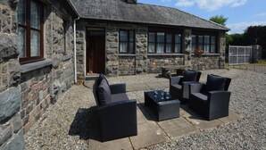 A stone building with a patio area featuring wicker furniture and a stone fireplace. - 3 Bed in Dolgellau (oc-75737) (Dolgellau)