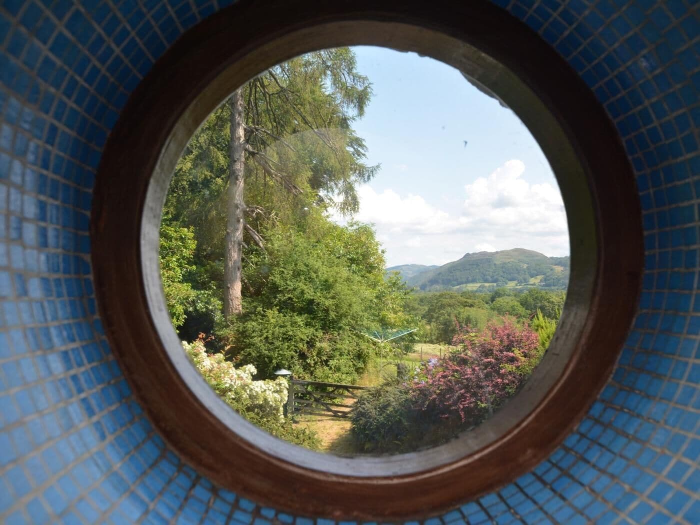 Una ventana circular con vistas a un paisaje exuberante, que incluye árboles y colinas.