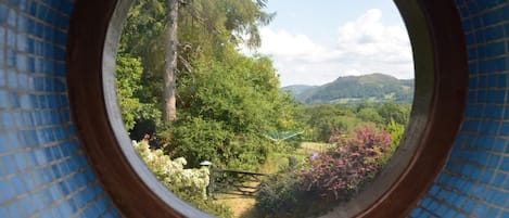A circular window with a view of a lush landscape, including trees and hills.