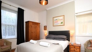 A bedroom with a bed, a wooden wardrobe, a nightstand, a chair, and a painting on the wall. - 2 Bed in Ventnor (oc-75730) (Ventnor)