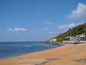 Une plage côtière avec un rivage rocheux, un ciel dégagé et des bâtiments situés sur le versant de la colline.
