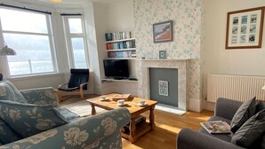A living room with a sofa, armchair, coffee table, fireplace, bookshelf, and a television. - 2 Bed in Ventnor (oc-75730) (Ventnor)
