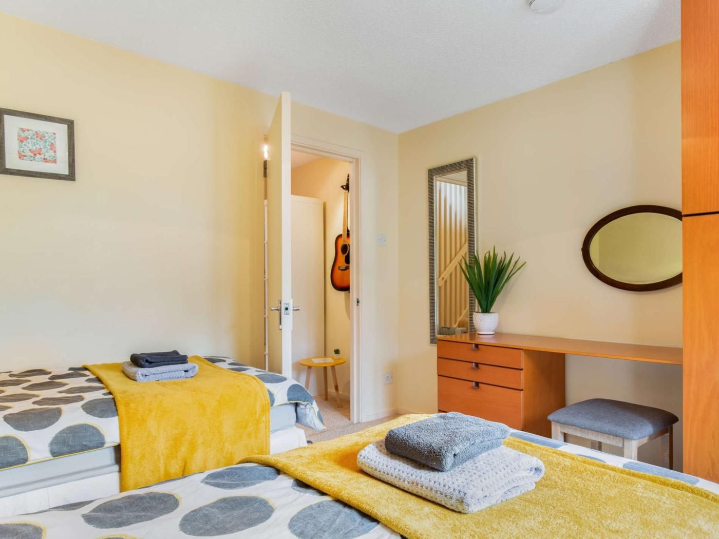 A bedroom with two beds, a dresser, a mirror, and a guitar in the background.