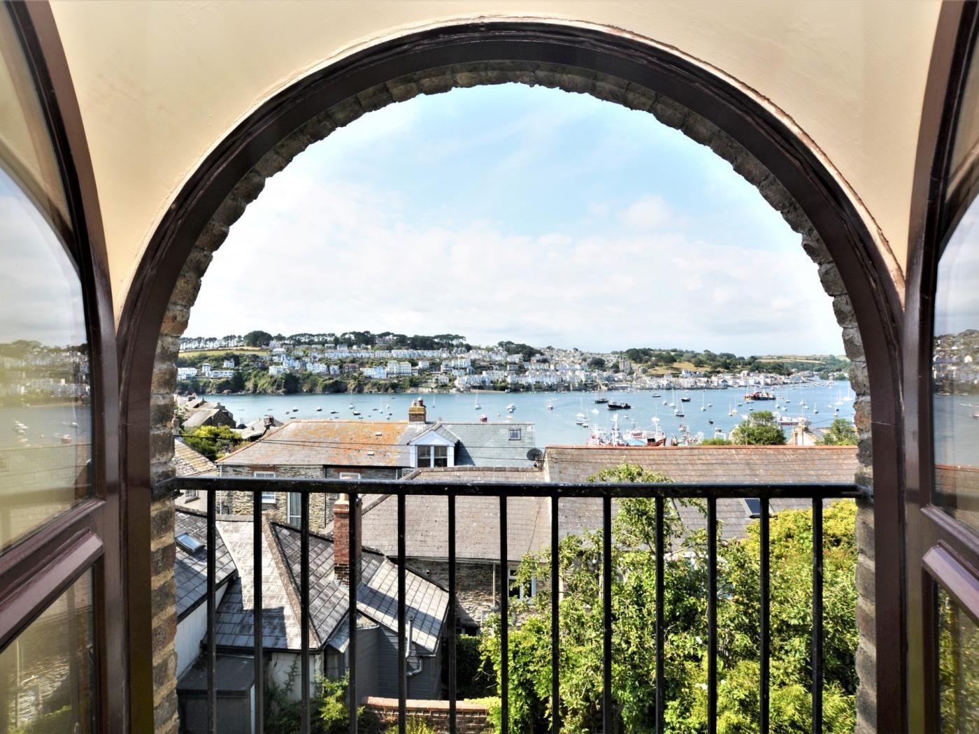 Una vista attraverso una finestra ad arco su una cittadina costiera, con barche sull'acqua e edifici sullo sfondo.