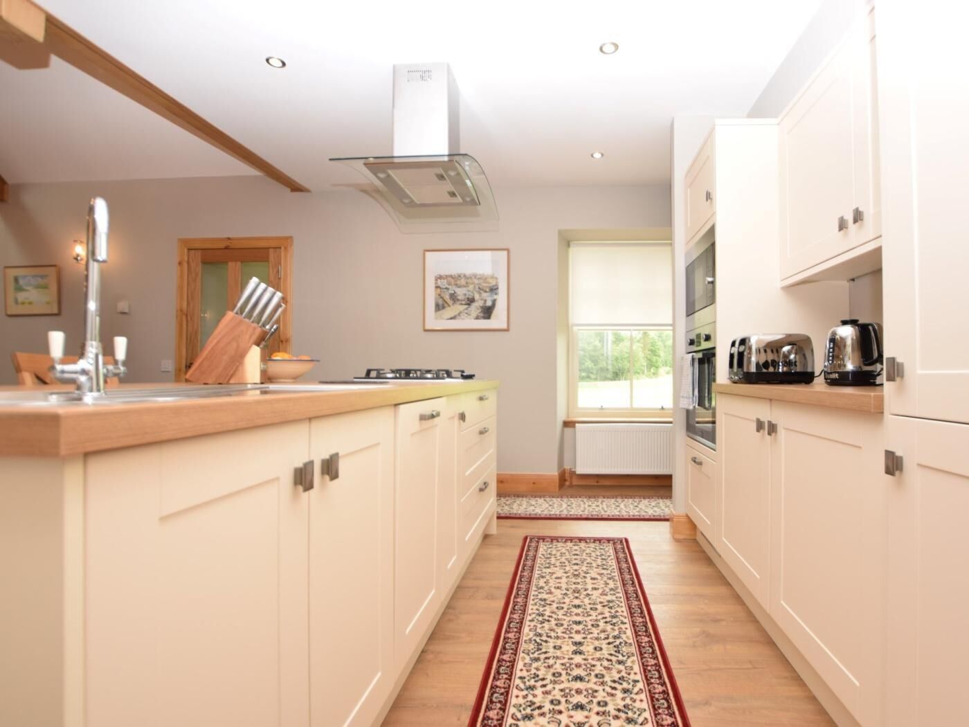 A kitchen with white cabinets, a wooden countertop, a gas stove, a sink, and a window with a view of greenery.