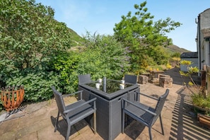 An outdoor patio with a table and chairs, surrounded by greenery and a stone wall. - 4 Bed in Wasdale (oc-sz326) (Wasdale)