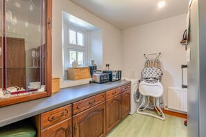 A compact kitchen with wooden cabinets, a countertop, a window, and a baby high chair. - 4 Bed in Wasdale (oc-sz326) (Wasdale)