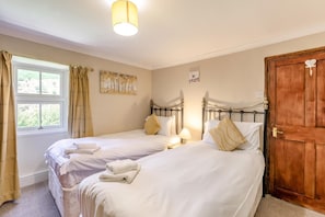 Une chambre avec deux lits simples, une porte en bois et une fenêtre avec des rideaux.