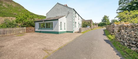 A two-story house with a paved driveway and a stone wall on one side.