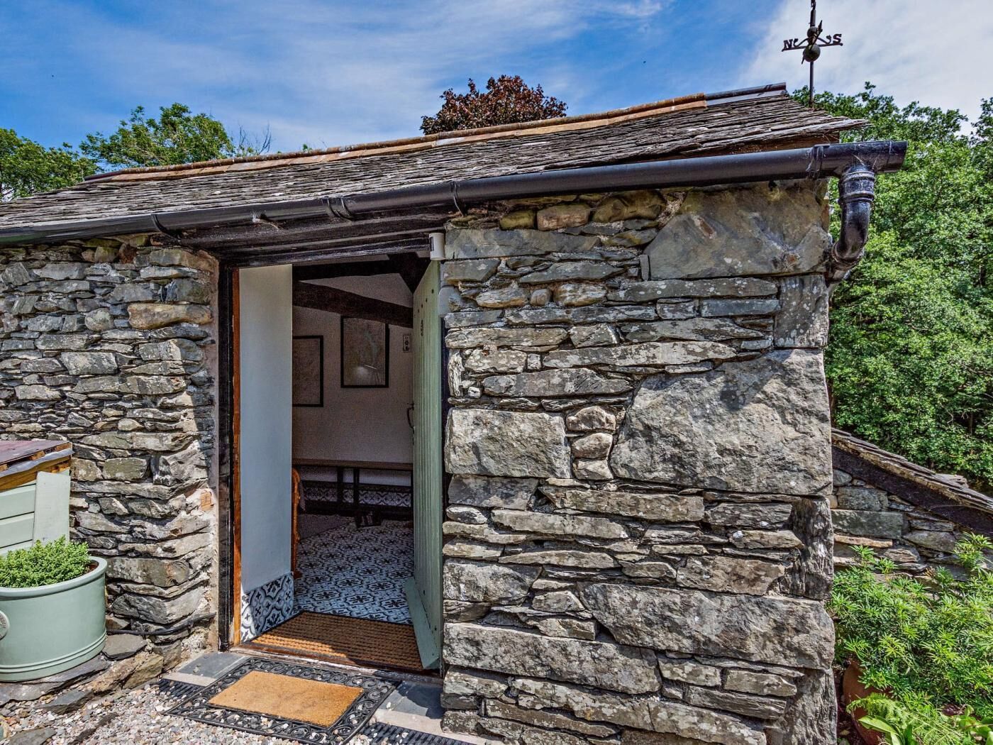 Ein Steinhaus mit offener Tür zu einem Zimmer, einer Steinmauer und einem kleinen Garten.