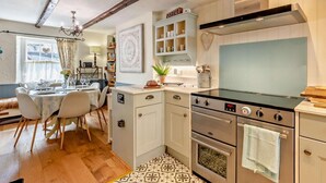 A kitchen with a stove, oven, and cabinets, a dining area with a table and chairs, and a ceiling with exposed beams. - 3 Bed in Ulverston (oc-sz445) (Satterthwaite)