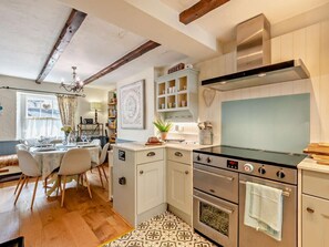Eine Küche mit Herd, Backofen und Schränken, ein Essbereich mit Tisch und Stühlen sowie eine Decke mit freiliegenden Balken.