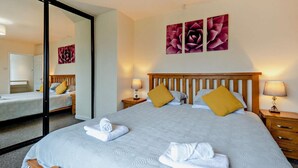 Hotelkamer met een groot bed, twee nachtkastjes, een spiegel en drie bloemschilderijen aan de muur.