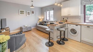 A compact kitchen with a washing machine, a dining area with a table and bar stools, and a sofa. - 1 Bed in Keswick (oc-85419) (Keswick)