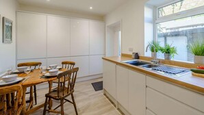 Una cocina moderna con comedor, muebles blancos, una mesa de madera y una ventana con plantas.