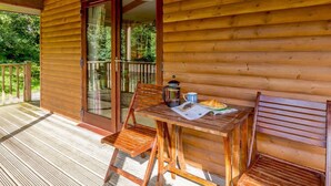 A wooden cabin with a balcony, a table with chairs, and a coffee pot. - 1 Bed in Holsworthy (oc-85561) (Bradworthy)