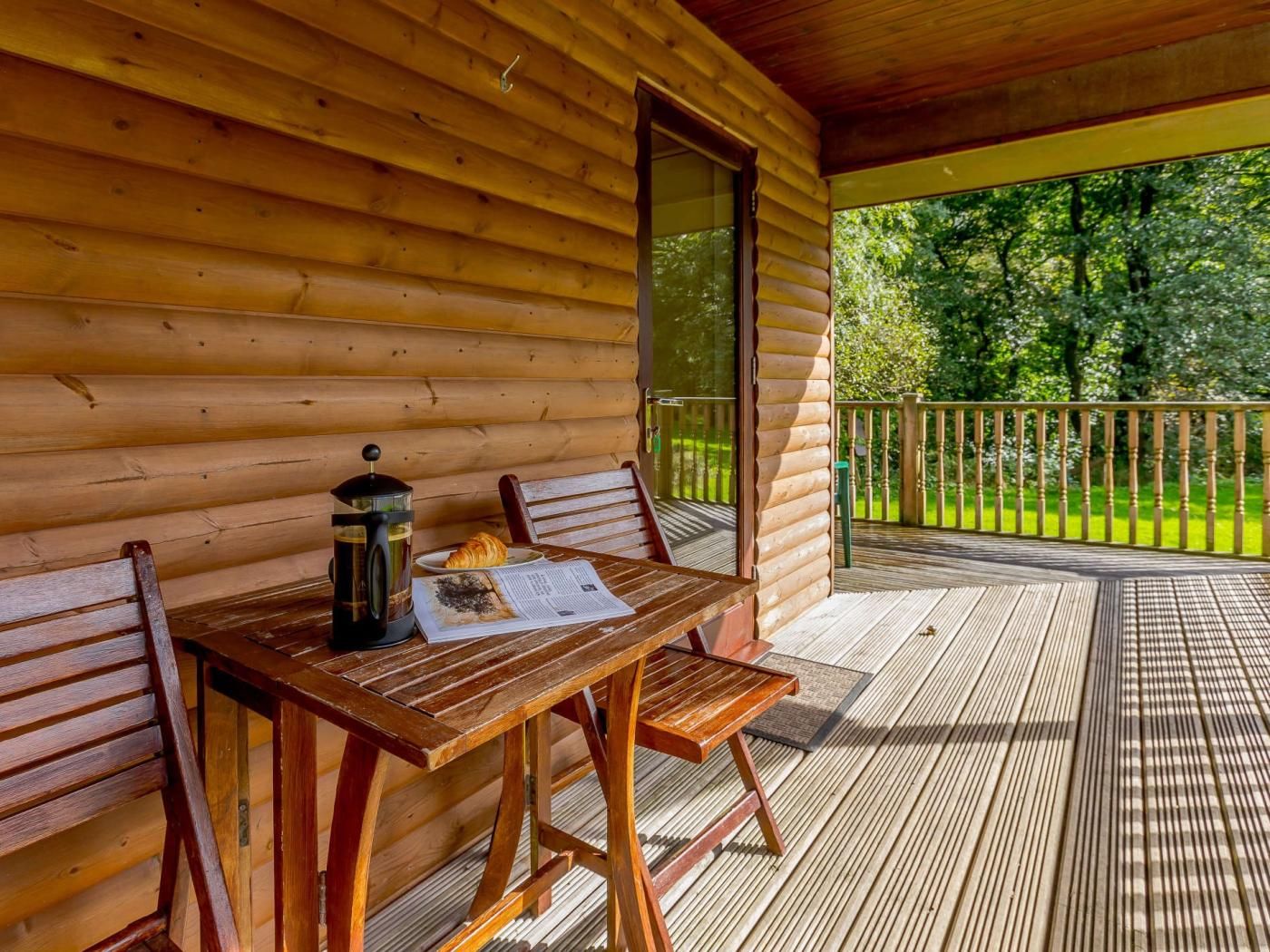 A wooden cabin with a deck, a table with chairs, a coffee pot, and a croissant.