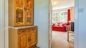A wooden cabinet with glass doors, a red sofa, and a lamp in a living room. - 2 Bed in Nairn (oc-ca144) (Nairn)