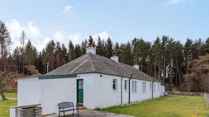 A white cottage with a green door, a small patio with a bench, and a garden. - 2 Bed in Nairn (oc-ca144) (Nairn)