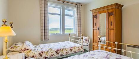 A bedroom with two beds, a wooden wardrobe, a window with curtains, and a hanging lamp.