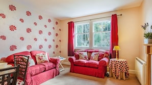 A cozy living room with two red sofas, a wooden chair, a small table with a polka dot tablecloth, and a window with red curtains. - 2 Bed in Nairn (oc-ca144) (Nairn)