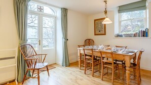 Ein Esszimmer mit Holztisch, gedeckt für vier Personen, mit zwei Stühlen, einem Fenster mit Vorhängen und einer Hängelampe.