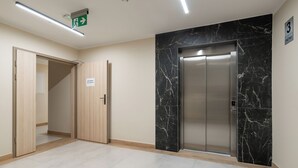 A modern elevator with a marble wall, a wooden door, and a sign indicating the floor. - SeaLight Apartment – Cozy Apartment in the Heart of Świnoujście (Swinemünde)