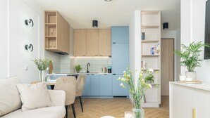 A modern kitchen with wooden cabinets, a blue refrigerator, and a dining area with a white table and chairs. - SeaLight Apartment – Cozy Apartment in the Heart of Świnoujście (Swinemünde)