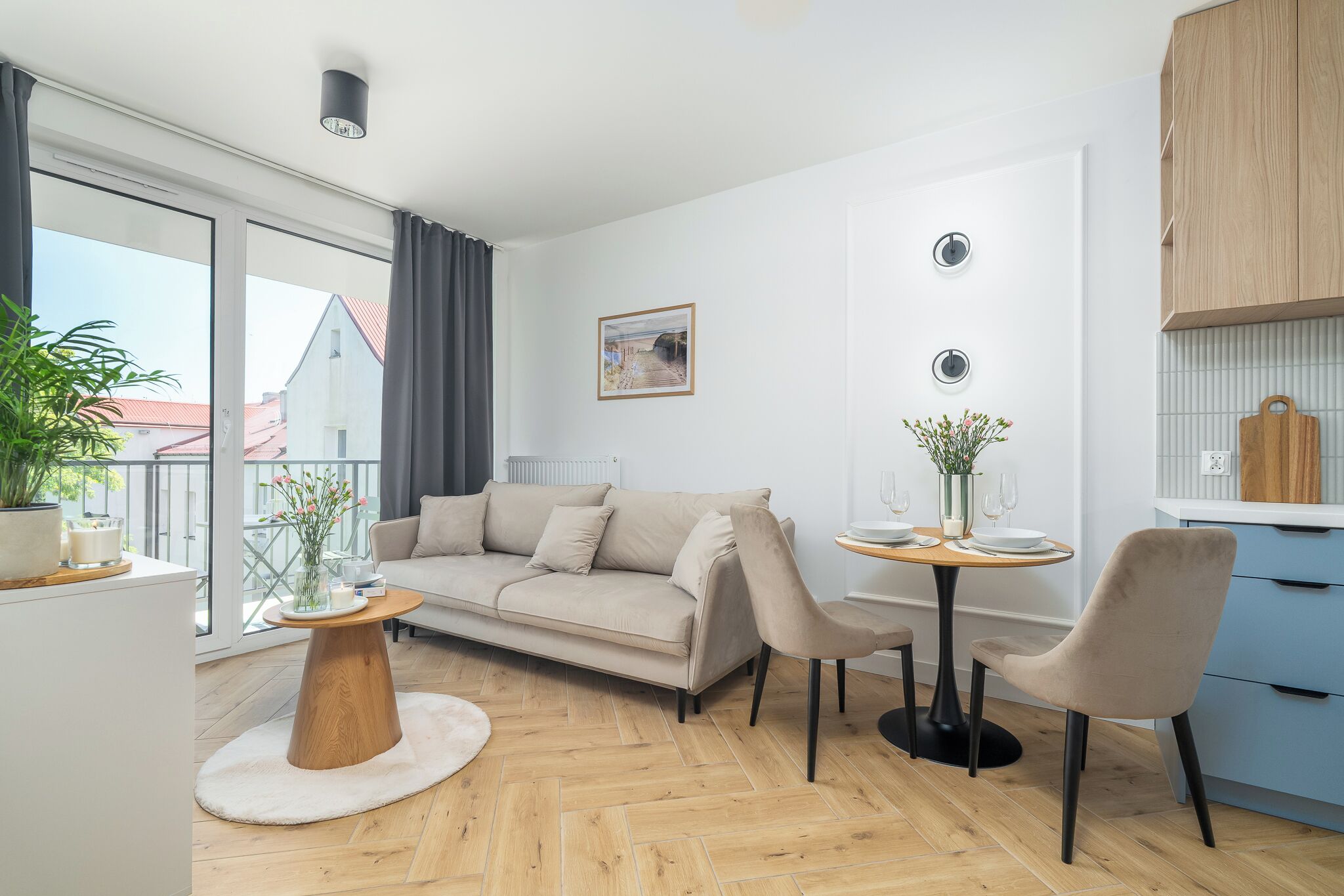 Ein modernes Wohnzimmer mit Sofa, Couchtisch und Sesseln, einem Esstisch mit Tellern und Gläsern, einer Topfpflanze und einem Gemälde an der Wand.
