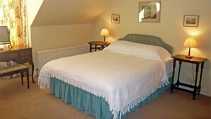 Un dormitorio con cama, dos mesitas de noche con lámparas, un aparador, un radiador y una ventana con cortinas.
