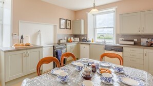 Une cuisine avec une table à manger dressée pour le petit-déjeuner, agrémentée d’une nappe à motifs et d’assiettes bleues et blanches.