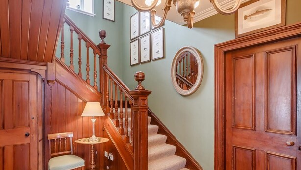 Un escalier en bois, un lustre, un miroir rond et des tableaux encadrés accrochés au mur.