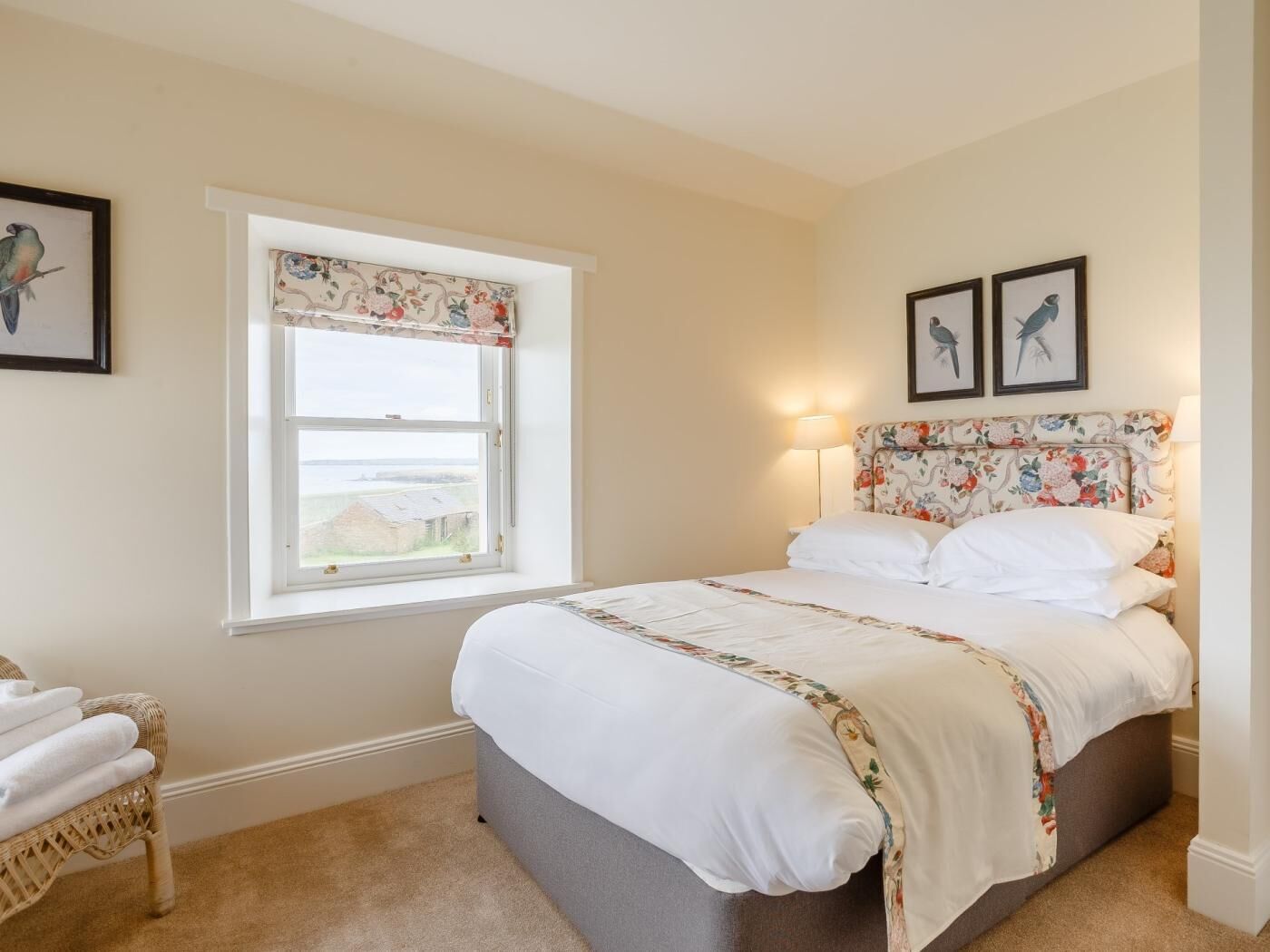 Een slaapkamer met een bed, een raam met uitzicht, een stoel en twee foto's in lijsten aan de muur.