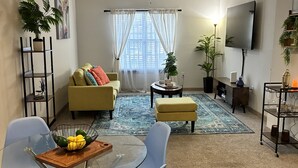 Una sala de estar con sofá, televisor, ventilador de techo y un comedor con sillas y mesa.