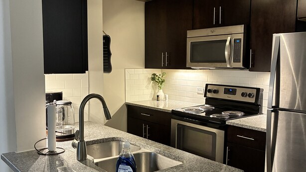 Una cocina moderna con gabinetes oscuros, electrodomésticos de acero inoxidable y una encimera de granito.