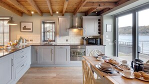 A modern kitchen with grey cabinets, a wooden ceiling, and a view of a lake. - 2 Bed in Inverness (oc-ca324) (Inverness)